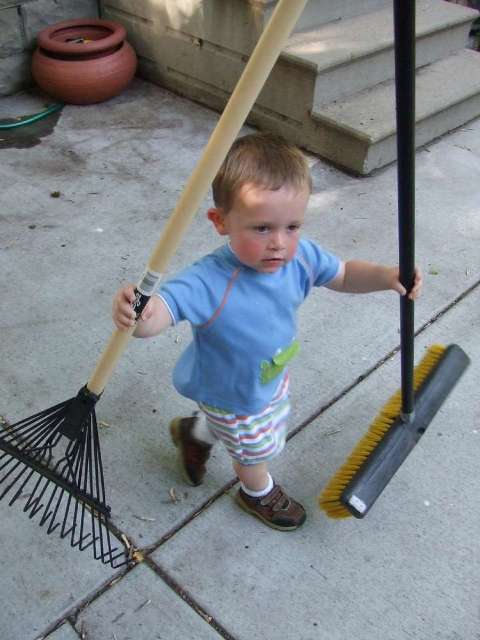 This toddler is ready for yardwork with a rake and broom!